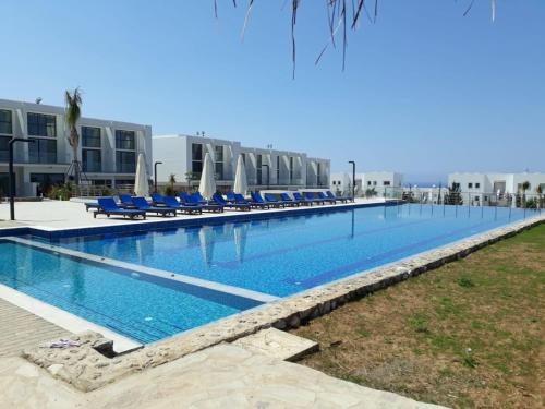 a large swimming pool with blue chairs and umbrellas at Retreat, block B1, unit15 in Küçükerenköy