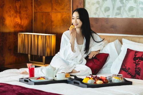 una mujer sentada en una cama con una bandeja de comida en Grand Millennium Al Wahda Hotel and Executive Apartments Abu Dhabi, en Abu Dabi