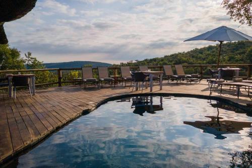a swimming pool with tables and chairs and an umbrella at Tshwene Lodge in Welgevonden Game Reserve