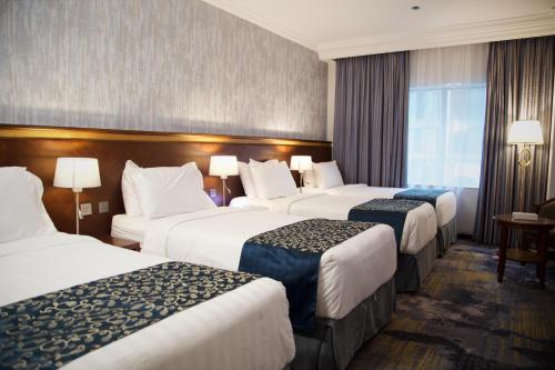 a hotel room with three beds and a window at Nozol Royal Inn Hotel in Al Madinah