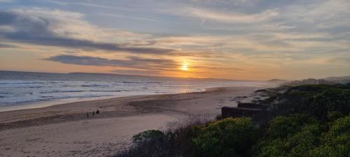 a sunset on a beach with people walking on the sand at Loerie Lane Accomadation in Groot Brak Rivier