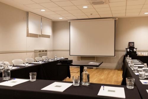 a conference room with tables and a large screen at Hotel PAX Torrelodones in Torrelodones