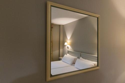a mirror reflecting a bed with white sheets and pillows at Hotel PAX Torrelodones in Torrelodones