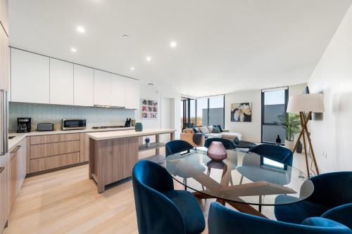 a kitchen and living room with blue chairs and a glass table at The Sapphire Nest - Spectacular Rooftop Amenities Ocean views 2BR in Los Angeles