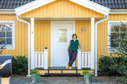 a woman standing on the front porch of a yellow house at Anettes Bed & Breakfast Falster in Eskilstrup