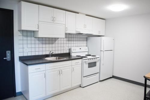 a kitchen with white cabinets and a white refrigerator at Residence & Conference Centre - North Bay in North Bay