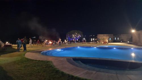 a swimming pool at night with people standing around at Sariska Kasba - A Village Resort in Tehla