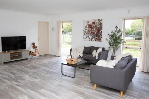 a living room with two couches and a flat screen tv at 2 Bedrooms with Garage right on Te Awa River Ride in Tamahere