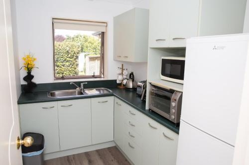a white kitchen with a sink and a microwave at 2 Bedrooms with Garage right on Te Awa River Ride in Tamahere