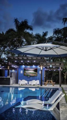 a pool with a blue umbrella and white chairs at Lake Of Dreams Miami House in Miami