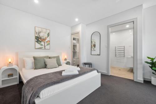 a white bedroom with a large bed and a mirror at Centrally Located Pymble Apartment in Pymble