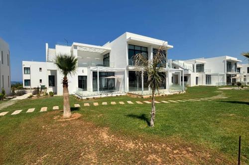 a large white house with a palm tree in front of it at Stylish apartment near the sea with direct pool access and top facilities in Ayios Nikolaos