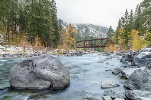 a river with rocks and a bridge in the background at Soaring Pines Lodge by NW Comfy Cabins in Leavenworth