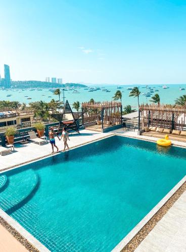 two people walking around a swimming pool with the ocean in the background at Hermann Hotel Pattaya in Pattaya