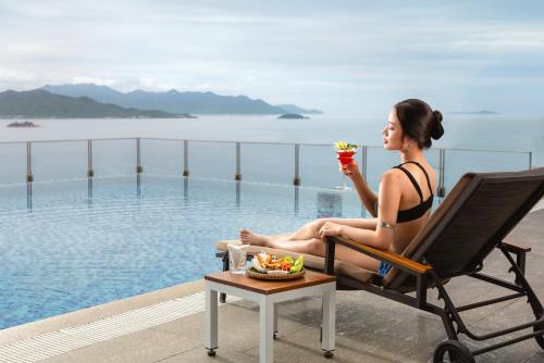 a woman sitting in a chair with a drink by the pool at Green Beach Hotel Nha Trang in Nha Trang