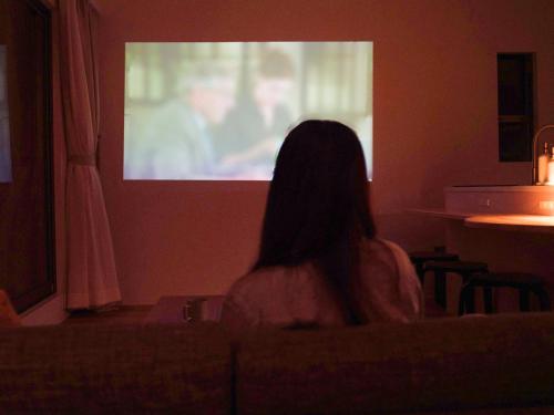 a woman sitting in a chair watching a movie on a screen at HOLLY CAMP CASA in Akagina