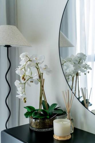 a table with a mirror and a lamp and white flowers at Nasma - Modern 3BR Oasis with Balcony in Azizi Riviera in Dubai