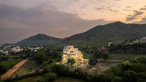 a building on a hill with mountains in the background at The Hills collective with private plunge pool My Downtown Hotel in Udaipur
