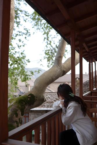 a woman sitting on a porch next to a tree at Armoloi Traditional - Guest House in Konitsa