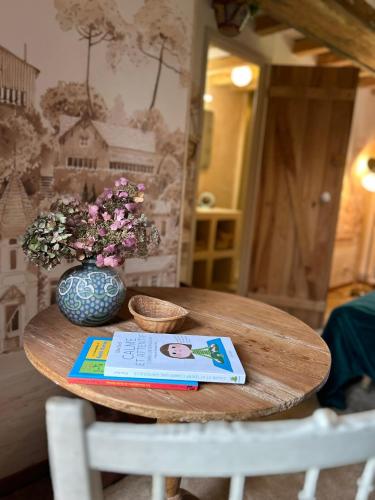 a table with a vase of flowers and a book at Gîtes et Spa en Normandie in Sainte-Marguerite-de-Viette