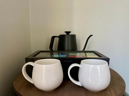 two white cups sitting on a table next to a coffee maker at Casa Azul - Off-grid Hideaway Agnes Water 1770 in Agnes Water
