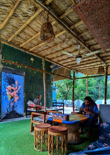 a man sitting at a table in a room with tables and stools at Hobbit House Hostel in Rishīkesh