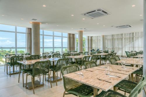 a dining room with tables and chairs and windows at Transamerica Dunas de Marapé in Jequia da Praia