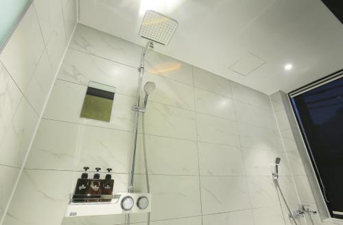a shower in a bathroom with white tiles at Zenith Hotel Bupyeong in Incheon