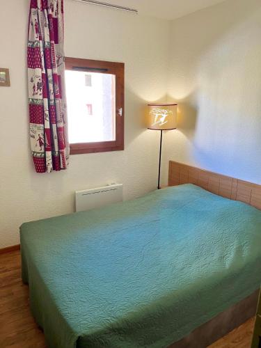 Un dormitorio con una cama con una lámpara y una ventana. en Appartement 5 personnes - Lumière des Neiges A 209, en Valmeinier