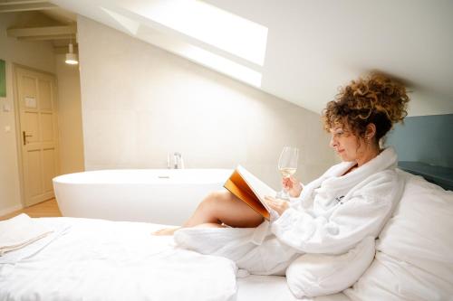 a woman sitting on a bed reading a book and drinking wine at Bohém Borklub in Tállya