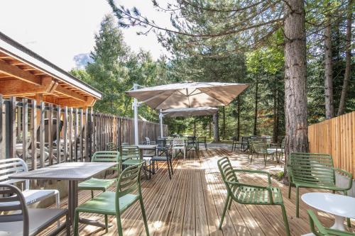 a deck with tables and chairs and an umbrella at VVF Les Écrins Saint-Léger-les-Mélèzes in Saint-Léger-les-Mélèzes