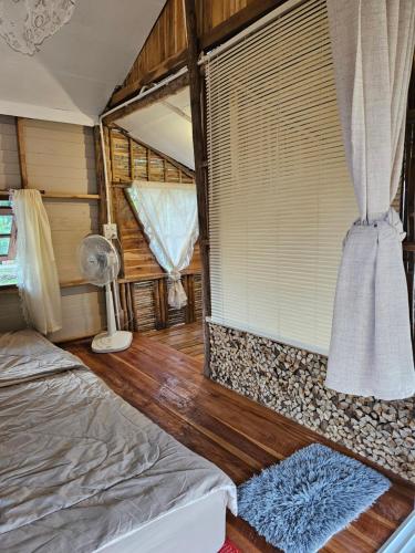 a bedroom with a bed and a window with a fan at PANAKLUEA Cottage & Crafts - พนาเกลือ in Ban Kham