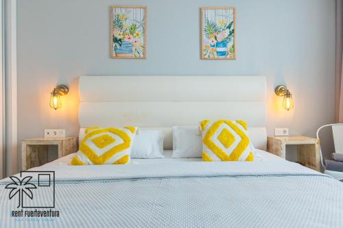 a bedroom with a bed with yellow and white pillows at Hola Jag Corralejo Center iRent Fuerteventura in Corralejo