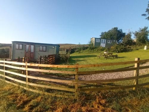 a fence in front of a yard with a caravan at The Herdsman Luxury Shepherds Hut in Barnoldswick