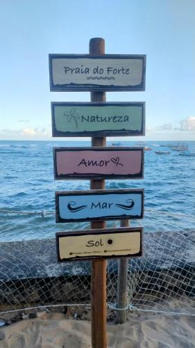a sign with several signs in front of the ocean at Pousada Du’Forte in Praia do Forte