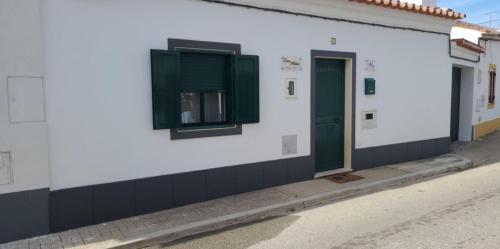 a white building with green windows and a street at Casa da Aldeia in Monsaraz