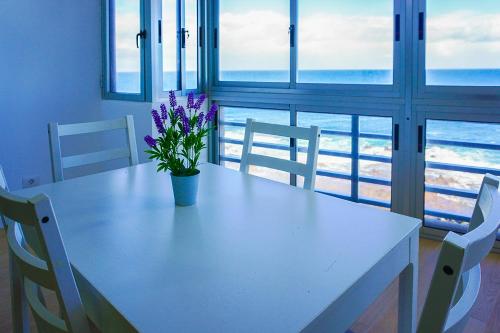 a white table with a vase with purple flowers on it at Apartamento frente al mar in Puertito de Güímar