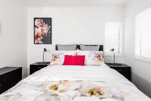 Un dormitorio blanco con una cama grande con almohadas rojas. en The Urban Escape Stylish 1-Bed in Prime Downtown, en Mount Maunganui