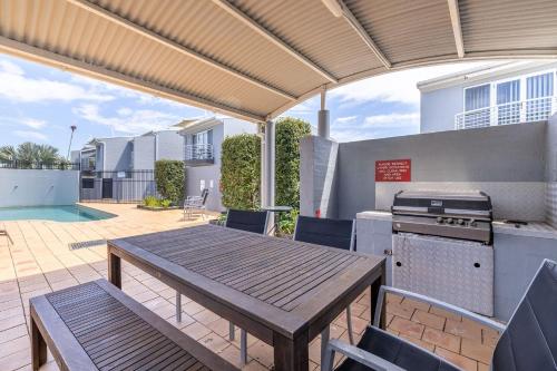 a patio with a wooden table and a grill at Sandcastles 4 -8 Ala Moana Way in Fingal Bay