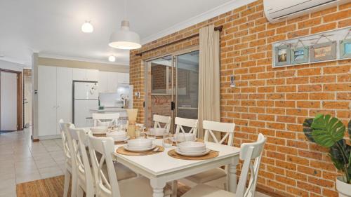 a dining room with a white table and a brick wall at Jervis Joy in Callala Beach