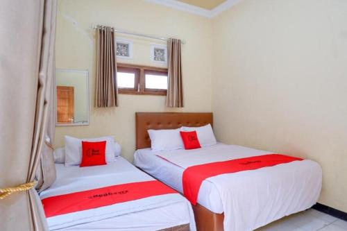 two beds in a room with red and white sheets at RedDoorz near Desa Wisata Tambi Dieng in Wonosobo