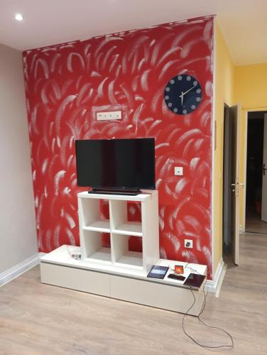 - une télévision sur un support devant un mur rouge dans l'établissement appartement, à Longeville-lès-Saint-Avold