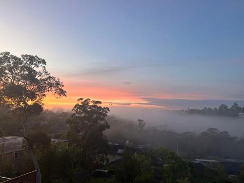 a misty sunrise with a view of a city at Family home in Mount Colah