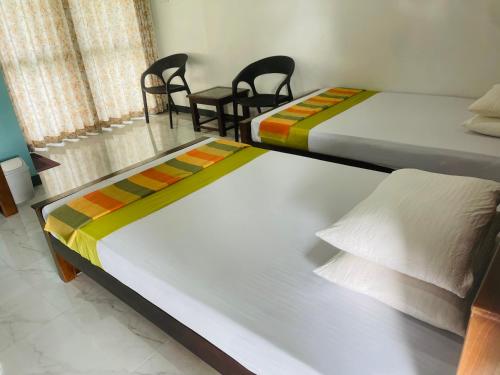 two beds in a room with two chairs and a table at Aura Villa in Polonnaruwa
