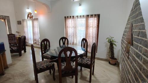 a dining room with a glass table and chairs at Flintstone Home in Kushālnagar