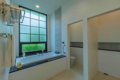 a bathroom with a tub and a window and a toilet at Villa Viola 7 Bedroom, Fully Staffed, on the Golf Course in Laguna Phuket