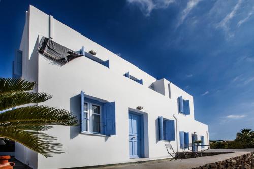a white building with blue windows and a palm tree at Astarti Apartments in Livadi