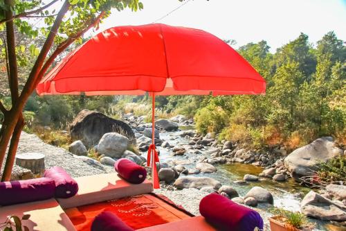 a red umbrella sitting on a beach next to a river at Prakriti Aalay - Riverside Mountain View Boutique Eco Resort in Dharamshala