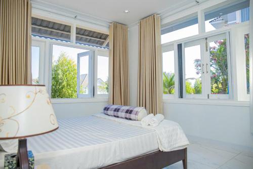 a bedroom with a bed with windows and a lamp at Sun House -Villa Sealink Phan Thiết - Mũi Né in Phan Thiet