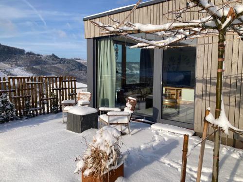 a house covered in snow with two chairs and windows at MoselHoch in Klüsserath